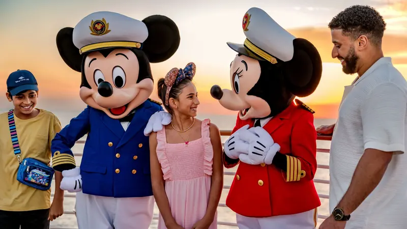 Mickey e Minnie vestidos de capitães ao lado de um casal, ao pôr do sol