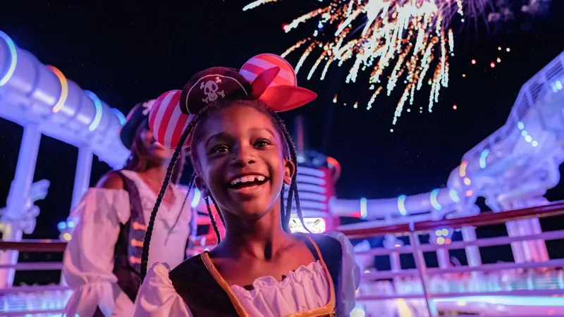 Menina sorridente com chapéu de pirata sob fogos de artifício no convés