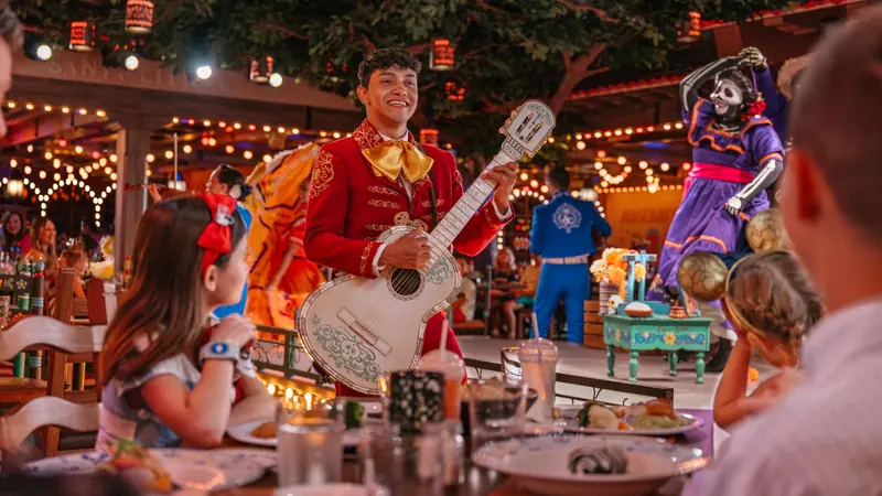 Família jantando enquanto um músico e personagens se apresentam à mesa