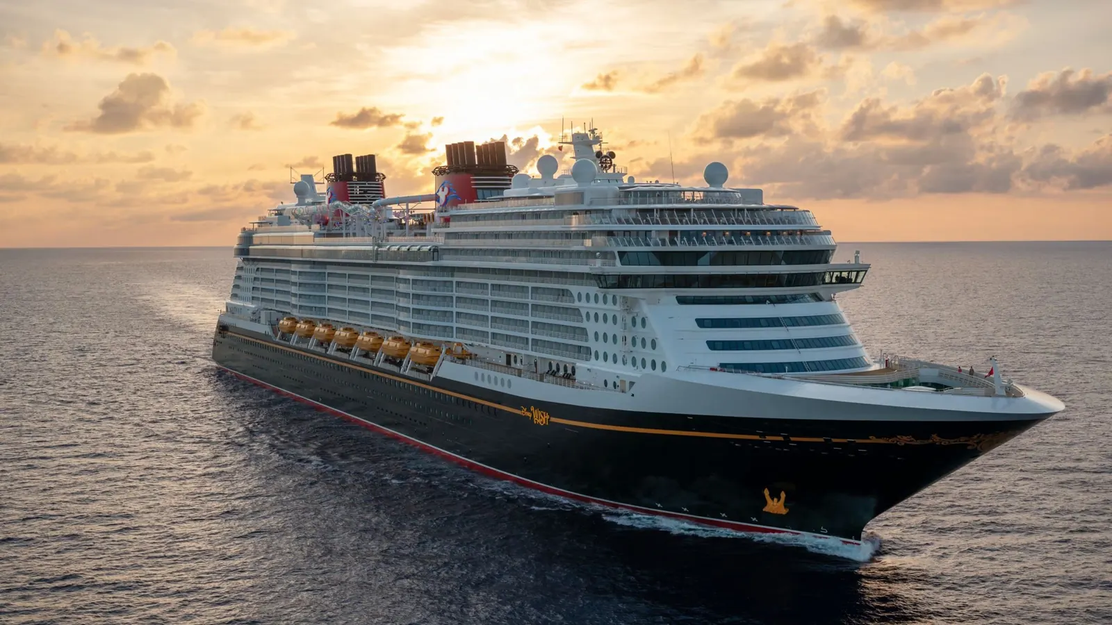 Vista aérea do navio Disney Wish ao entardecer, com o mar e o céu em tons dourados