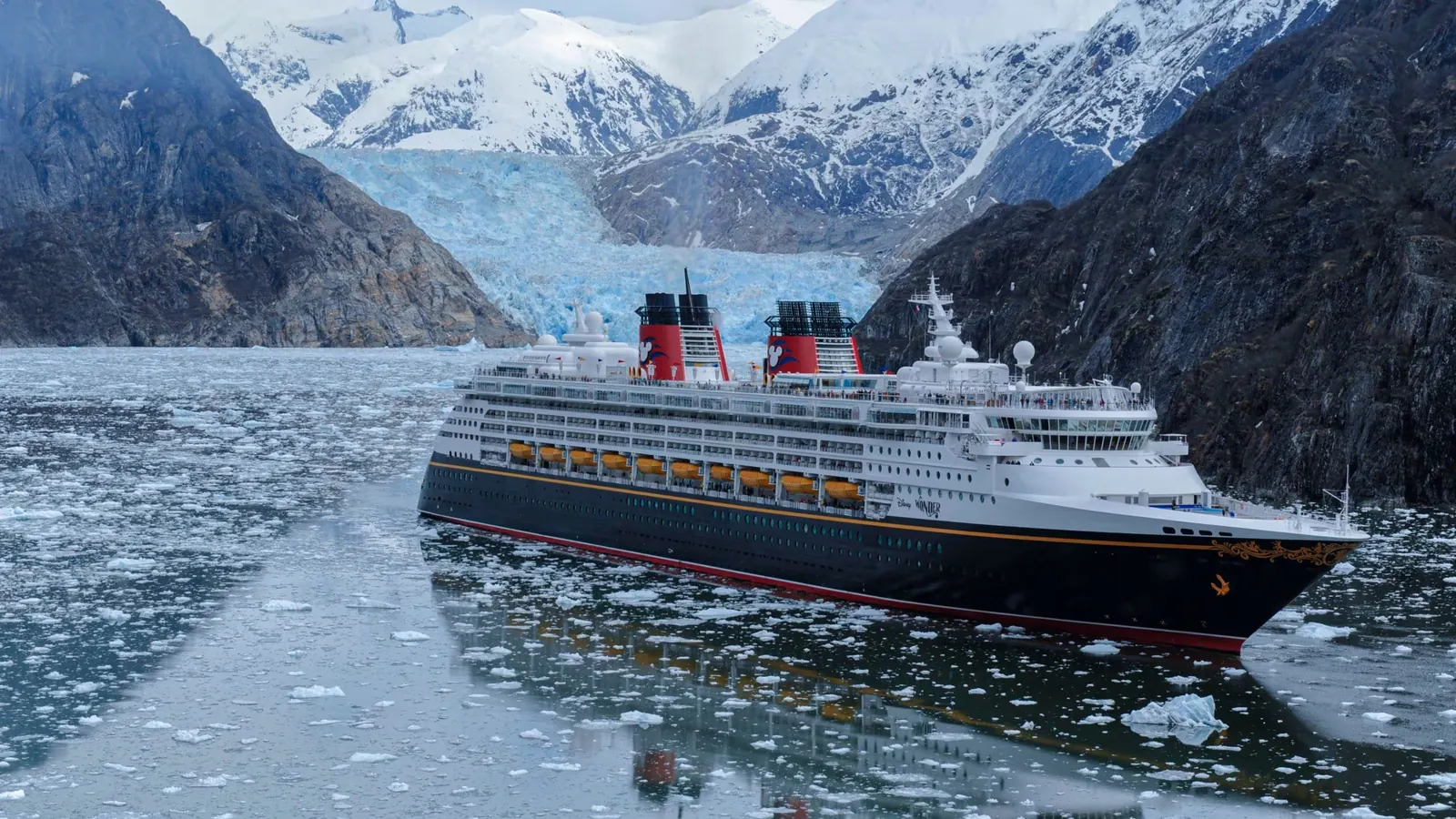 Vista aérea do navio Disney Wonder navegando entre gelo e montanhas nevadas do Alasca